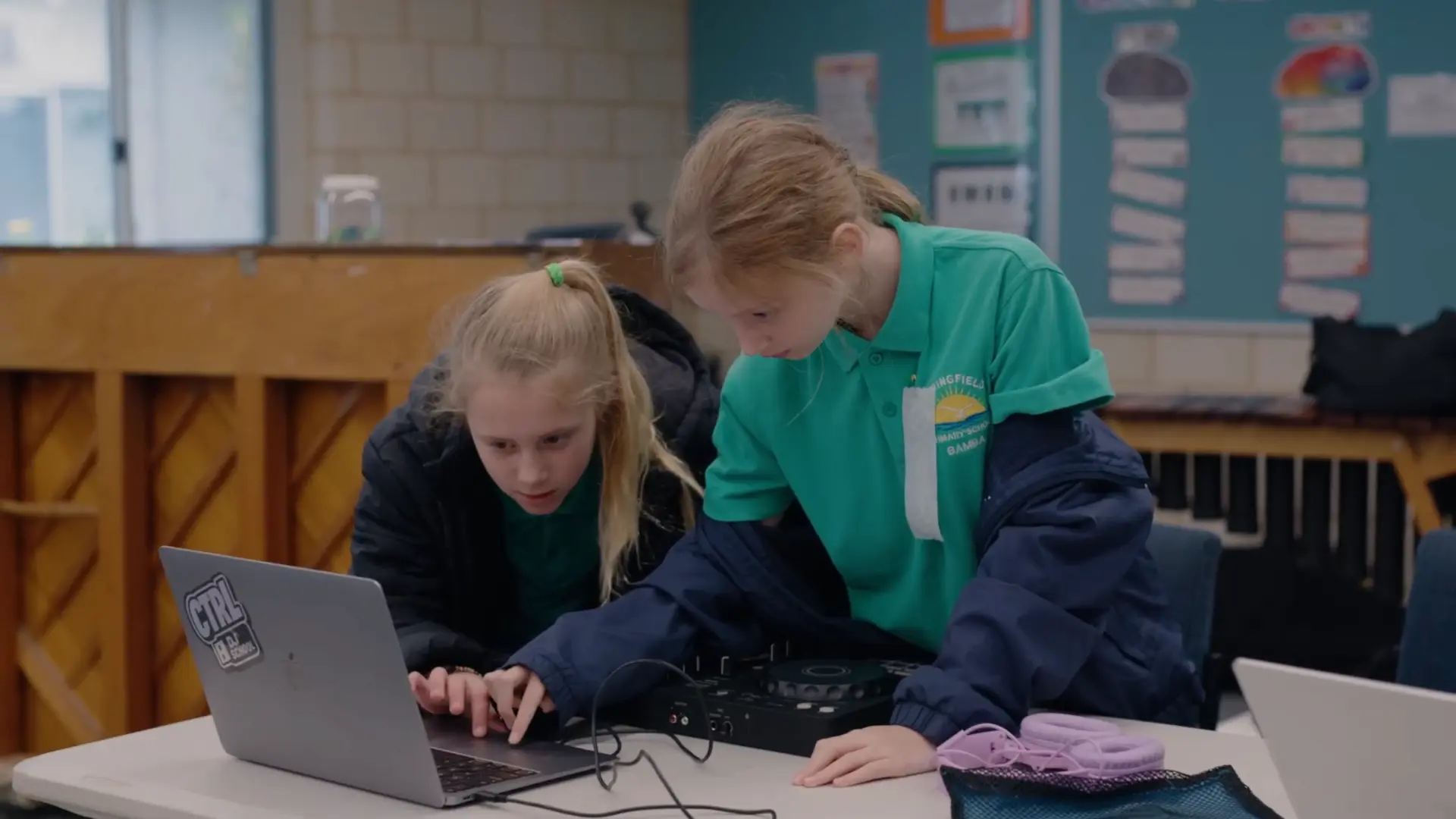 Two students collaborating on a laptop and DJ controller in the classroom